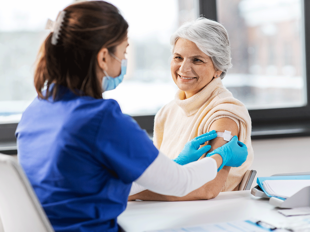 Smiling woman sitting while a medical worker applies an adhesive bandage to her arm